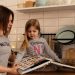 A mother and daughter enjoy reading a cookbook in a modern kitchen, sharing fun and learning together.